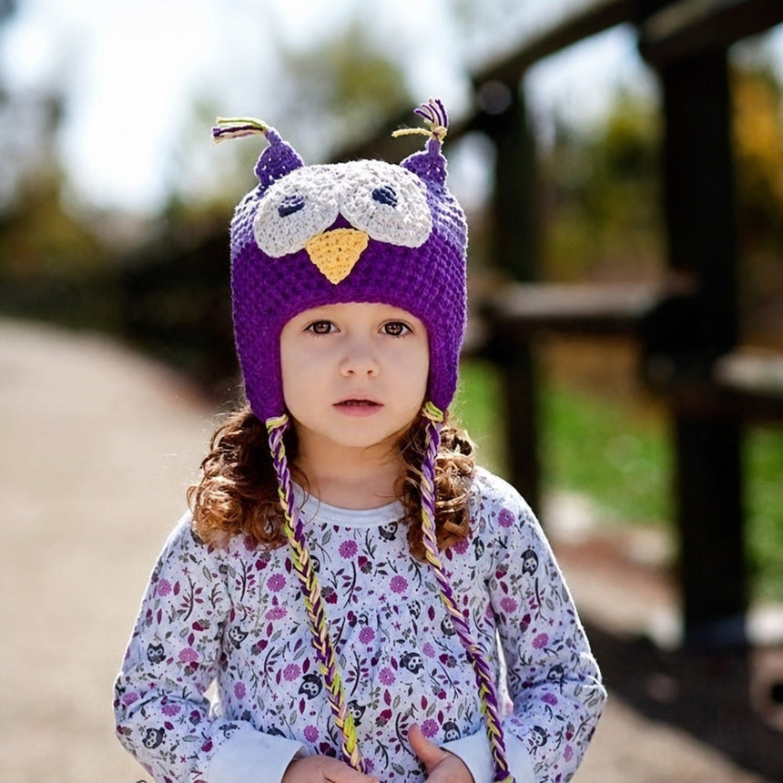 Child wearing light purple and purple owl beanie hat outdoors