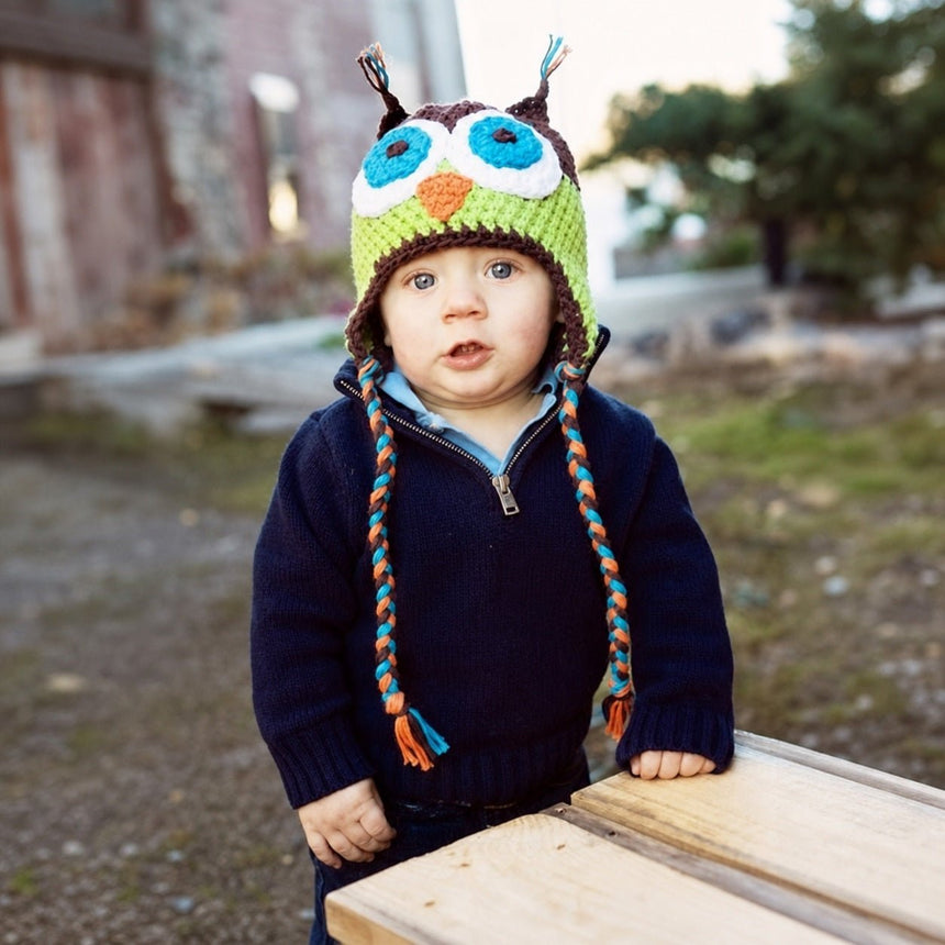 Child wearing brown and green crochet owl beanie with braided earflap ties