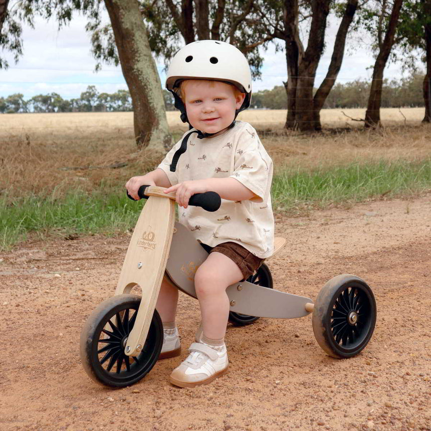 Toddler in a helmet riding the Kinderfeets Tiny Tot Plus Slate Grey trike on a dirt track