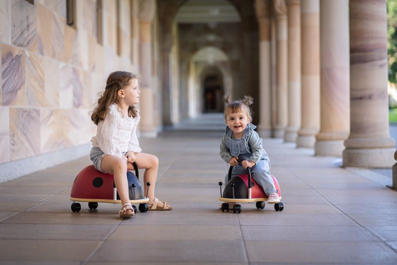 Two young girls sitting on Wheely Bug Ride On Ladybug ride-on toys facing each other outdoors