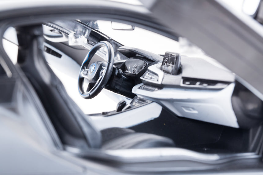 Detailed interior close-up of the Rastar 1:14 BMW i8 RC car with butterfly door open, showing the BMW steering wheel, detailed dashboard with digital display, centre console, and sculpted door panel.