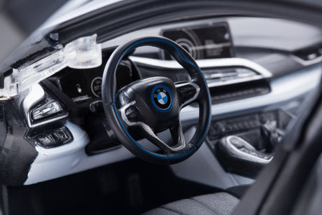 Close-up detail shot of the Rastar 1:14 BMW i8 RC car interior, showing the detailed BMW-branded steering wheel with blue trim, dashboard instruments, and centre console through the open butterfly door.