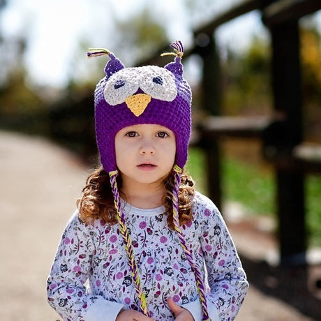 Child wearing light purple and purple owl beanie hat outdoors