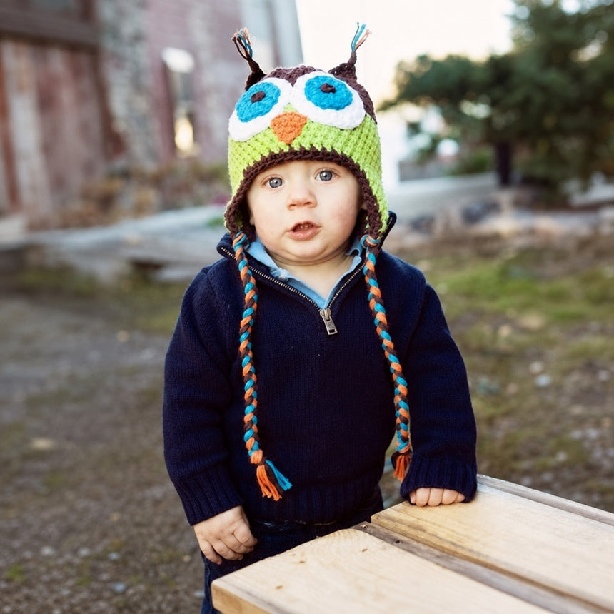 Child wearing brown and green crochet owl beanie with braided earflap ties
