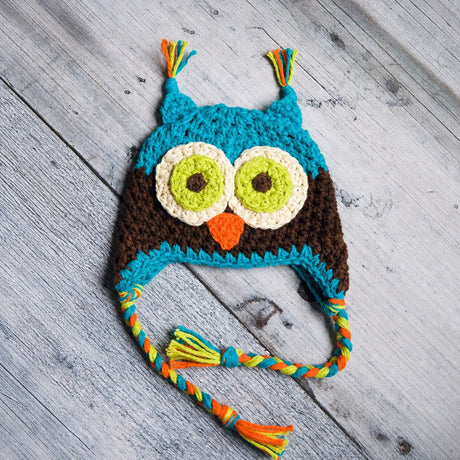 Blue and coffee owl beanie with braided ties on pale wood background