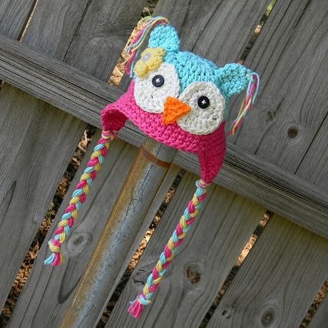 Light blue and rose owl beanie with braided ties on wooden background
