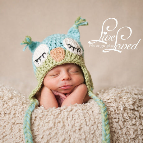 Baby wearing light blue and light green owl beanie with braided ties