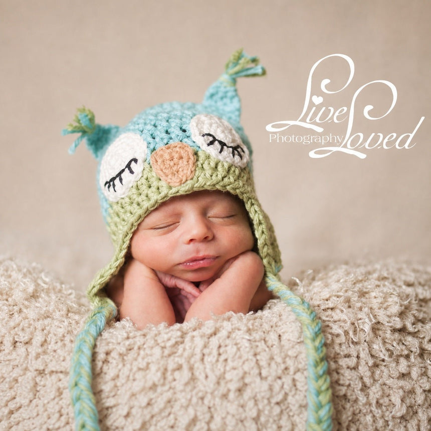 Baby wearing light blue and light green owl beanie with braided ties