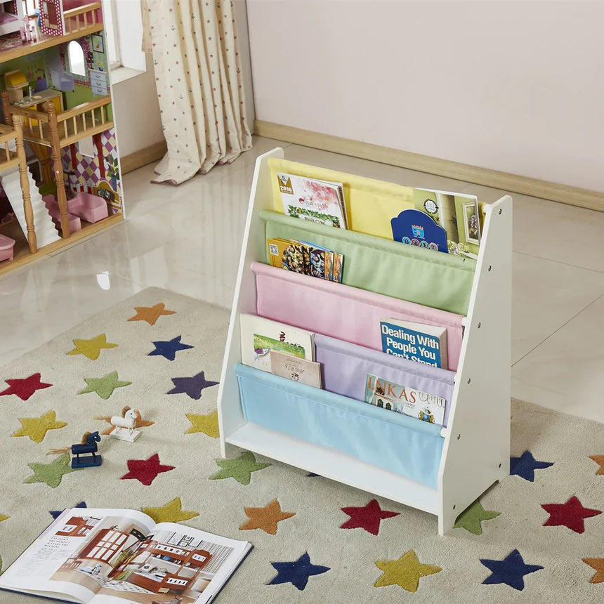 White wooden kids sling bookcase holding picture books, styled beside a dollhouse in a playroom