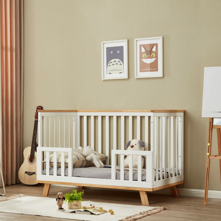 Modern wooden toddler bed with side rails in a cozy nursery, stuffed toys inside crib