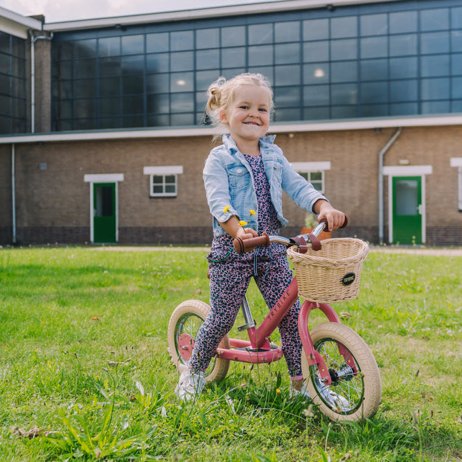 Child riding the Vintage Pink Trybike balance bike outdoors
